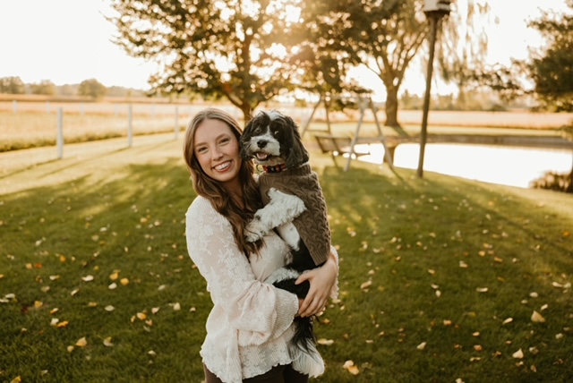 Erika smiling outdoors while holding a black-and-white dog.